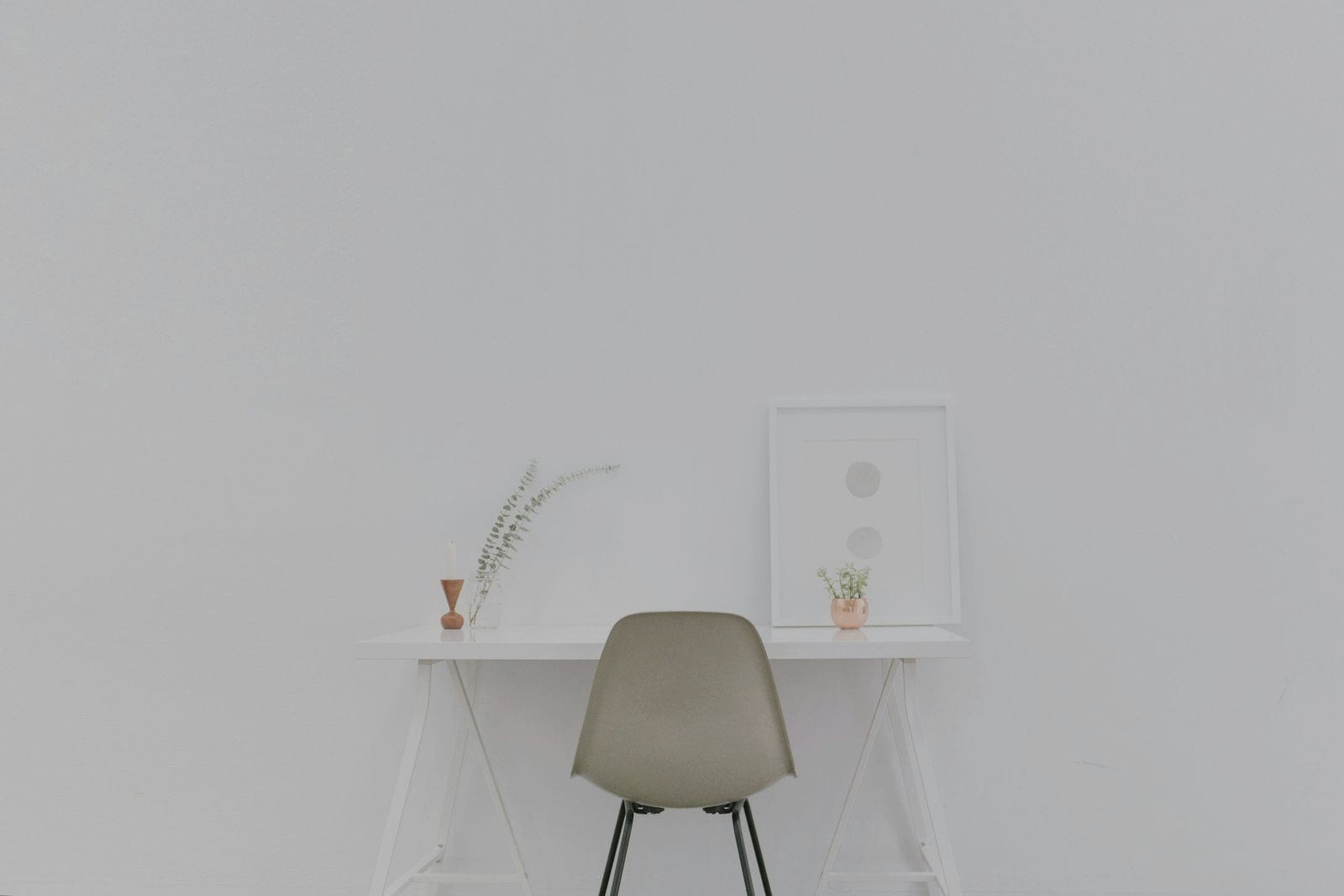 A pale desk and chair against a white wall, lit from one side